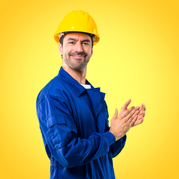 Young workman with helmet applauding after presentation in a conference on yellow background - Photo, Image