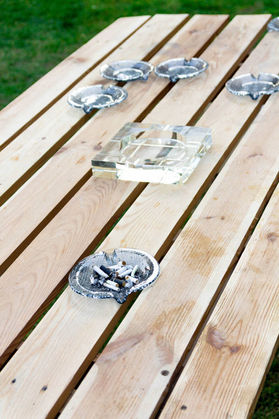 Glass ashtray on a wooden table. Ashtray with cigarette butts. - Photo, Image
