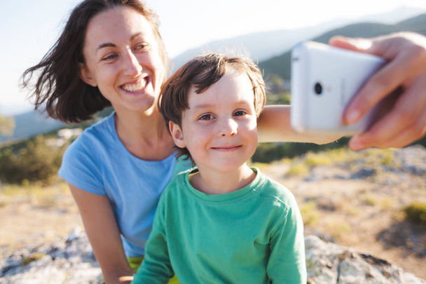 Een vrouw met een jongen op de top van een berg. Moeder en haar zoon maken selfie op de achtergrond van een prachtig landschap. Reizen met een kind. - Foto, afbeelding