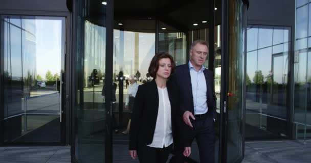 Two business people leaving building through spinning door and talking - Felvétel, videó
