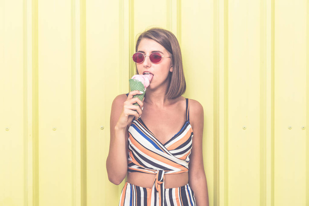 Hipster girl eating ice cream against yellow wall on the street. - Foto, Imagem