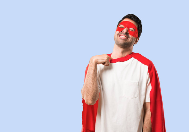 Superheld man met masker en rode cape met moe en ziek uitdrukking op geïsoleerde blauwe achtergrond - Foto, afbeelding