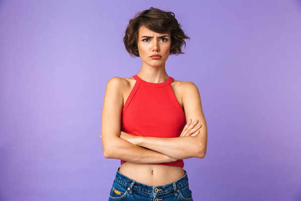 Image closeup of young displeased woman 20s in casual wear frowning and standing with arms folded isolated over violet background - 写真・画像