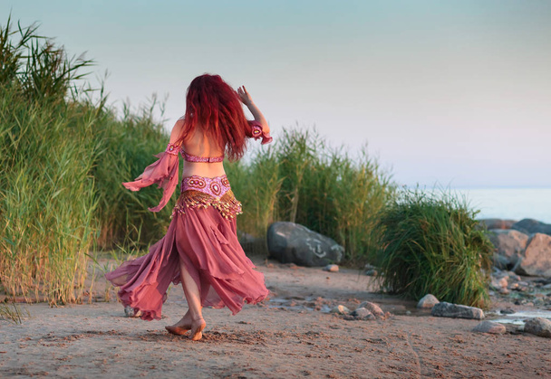 Beautiful young woman in Oriental dance costume by the sea. Expensive costume decorated with rhinestones and beads. Dancing girl on the seashore. - Photo, Image