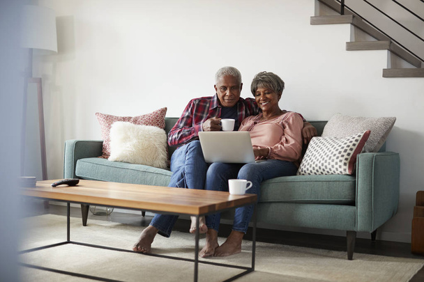Senior Couple Sitting On Sofa At Home Using Laptop To Shop Online - Foto, immagini