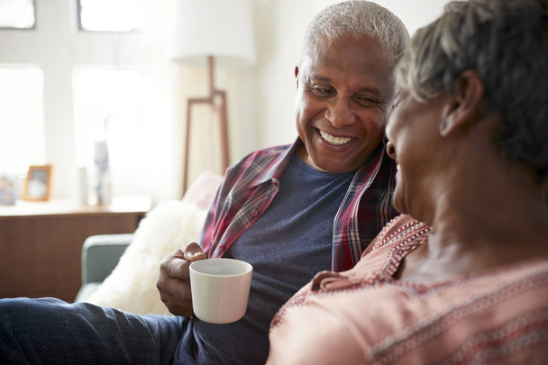 Senior Couple Sitting On Sofa At Home Relaxing With Hot Drink - Photo, image