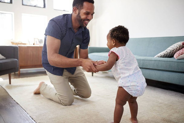 Father Encouraging Baby Daughter To Take First Steps At Home - Φωτογραφία, εικόνα