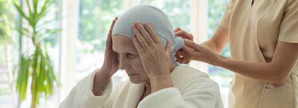 Panorama of caregiver putting scarf on elderly woman's head during chemotherapy - Фото, изображение