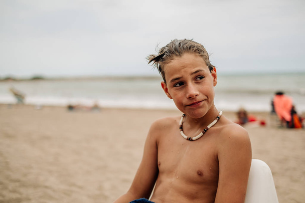 Мокрый серьезный мальчик сидит на пляже и думает:
 - Фото, изображение