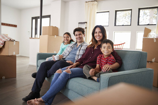 Happy Family Resting On Sofa Surrounded By Boxes In New Home On Moving Day - Photo, image