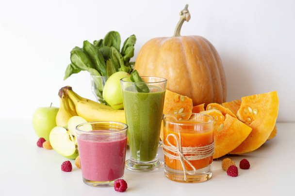 Smoothies de legumes e frutas outonais em um fundo branco ao lado de abóbora, espinafre, banana, framboesas e maçãs. Dieta, Desintoxicação e Alimentos Vegetarianos
 - Foto, Imagem