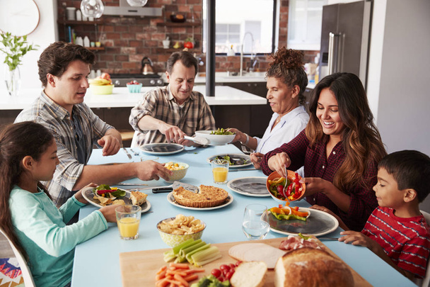 Familia multigeneracional disfrutando de la comida alrededor de la mesa en casa juntos
 - Foto, imagen