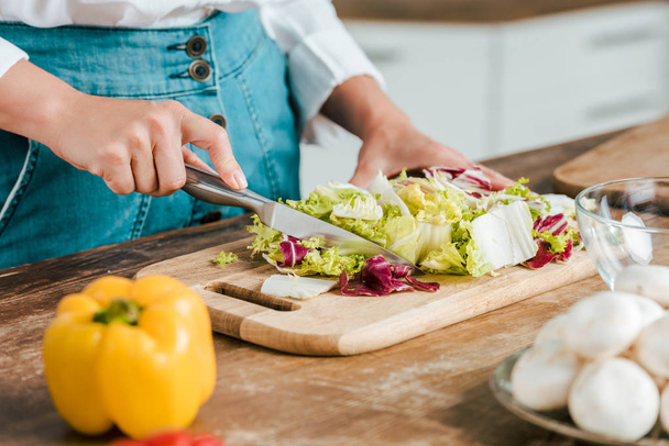 cropped shot of woman cutting lettuce for salad on wooden cutting board - 写真・画像