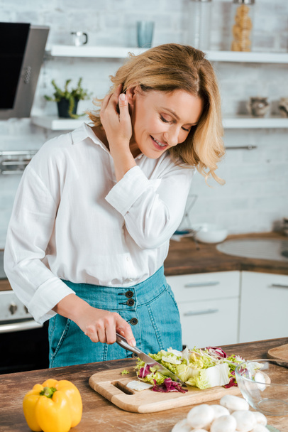 happy adult woman cutting lettuce for salad at kitchen - Foto, Imagen