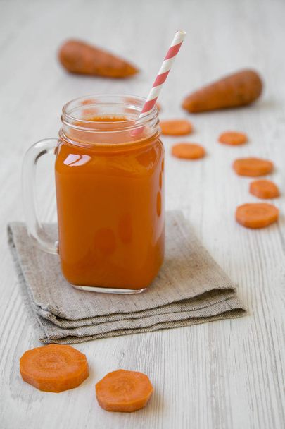Glass jar of carrot smoothie on white wooden surface, side view. Closeup. - Foto, Imagem