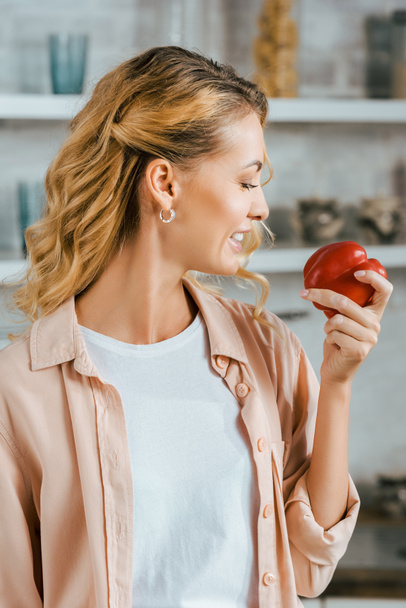 attractive young woman holding red ripe bell pepper at kitchen - Foto, Bild