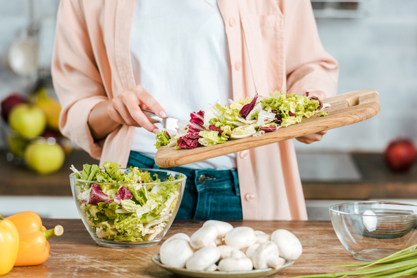 cropped shot of woman pouring cut lettuce into bowl from cutting board - Фото, зображення