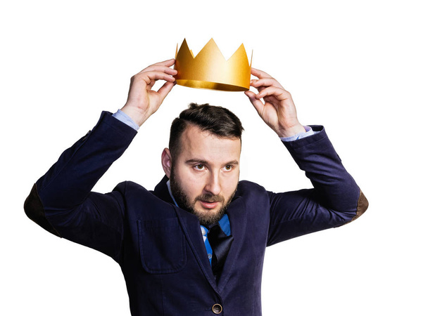 The concept of leadership, excellence. A portrait of a bearded man, he dresses a golden crown on his head. Isolated on white background. - Photo, Image
