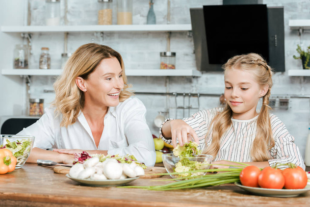 beautiful adult mother and little daughter cooking together at home - Foto, afbeelding