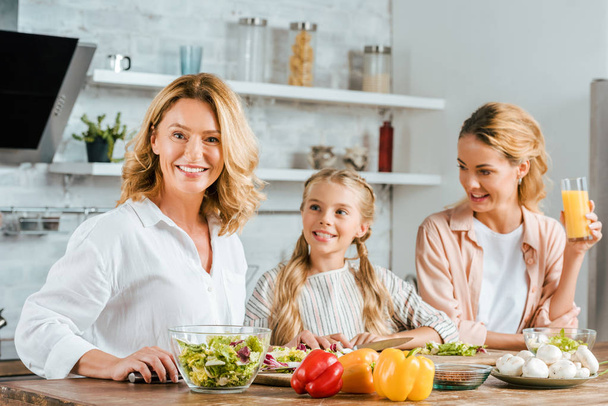 adult woman cutting vegetables for salad with daughter and granddaughter at home - Valokuva, kuva