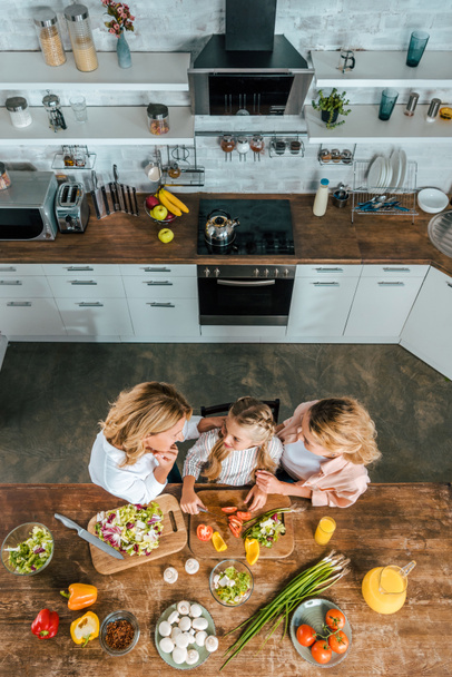 overhead view of child cutting vegetables for salad with mother and grandmother at kitchen - Foto, Bild