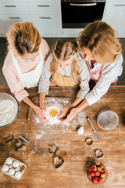 top view of child with mother and grandmother making dough with flour and egg together at home - Foto, Imagem