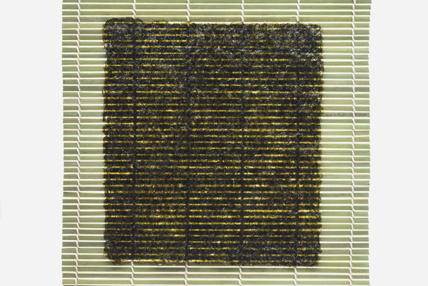 κάτοψη του nori φύλλο στο μπαμπού χαρτοπετσέτα ρολού απομονωθεί σε λευκό - Φωτογραφία, εικόνα