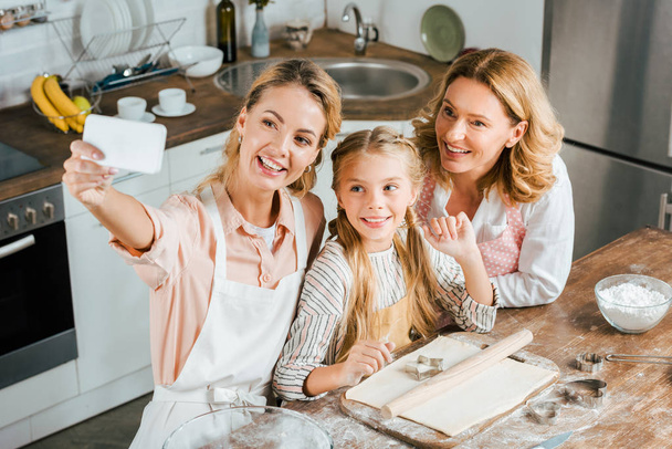 hoge hoekmening van vrouw nemen selfie met haar moeder en dochter tijdens het koken thuis - Foto, afbeelding