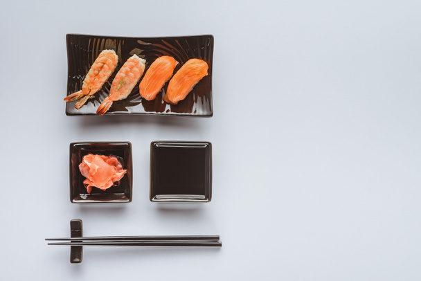 top view of delicious sushi with salmon and shrimp, ginger, soy sauce and chopsticks isolated on white  - Фото, изображение