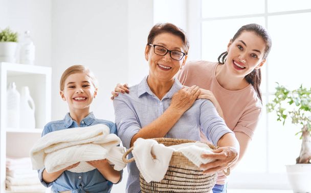 Beautiful women and child girl little helper are having fun and smiling while doing laundry at home. - Foto, imagen