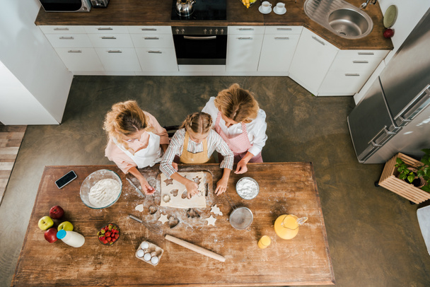 vue du dessus de l'enfant avec la mère et la grand-mère couper la pâte pour les biscuits de Noël à la maison
 - Photo, image