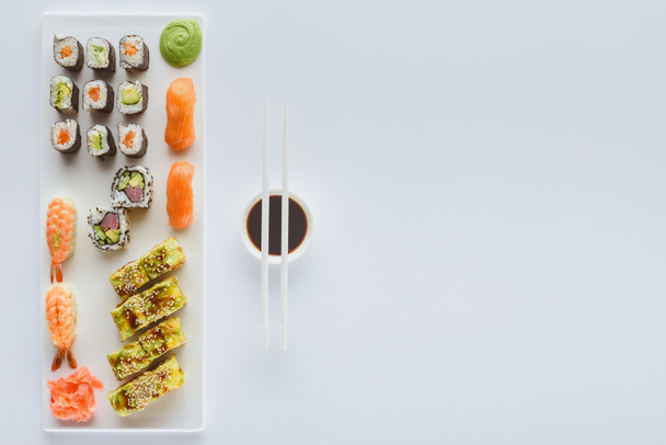 top view of delicious sushi set and soy sauce in bowl with chopsticks isolated on white background  - Fotoğraf, Görsel