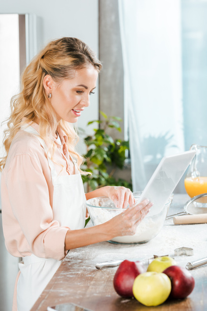 attractive young woman making dough and using tablet at home - Foto, Bild