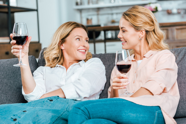 щаслива зріла мати і доросла дочка в келихах червоного вина проводять час разом вдома
 - Фото, зображення