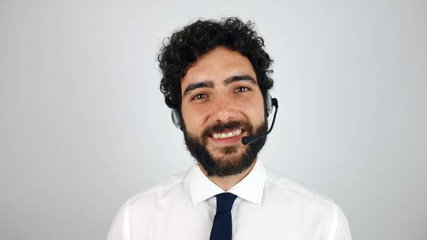 gutaussehender Berater eines Callcenters mit Kopfhörern auf grauem Hintergrund. junger und brünetter Mann lächelt in die Kamera. - Foto, Bild