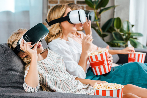 pieni lapsi äiti ja isoäiti istuvat sohvalla yhdessä ja katsovat elokuvan virtuaalitodellisuus kuulokkeet kotona
 - Valokuva, kuva
