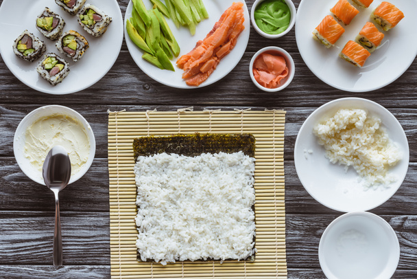 bovenaanzicht van rijst, nori en ingrediënten voor sushi op houten tafel - Foto, afbeelding