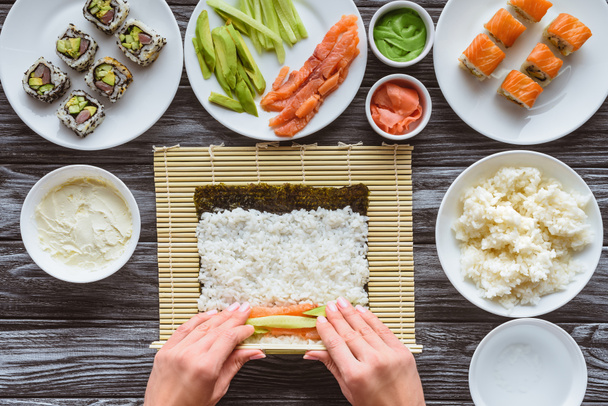 tiro cortado de pessoa preparando sushi com arroz, nori, salmão e abacate
  - Foto, Imagem