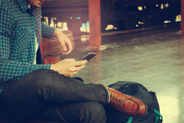 Asiatique hipster homme tenant téléphone mobile en utilisant app chanson avec de la musique de linteau à la gare
. - Photo, image