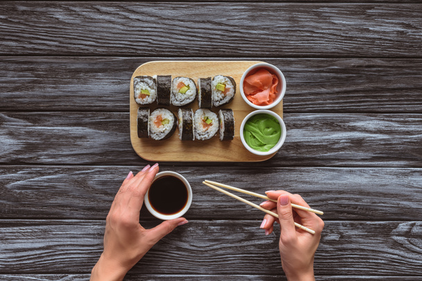 tiro cortado de pessoa segurando pauzinhos e tigela com molho de soja enquanto come sushi
  - Foto, Imagem