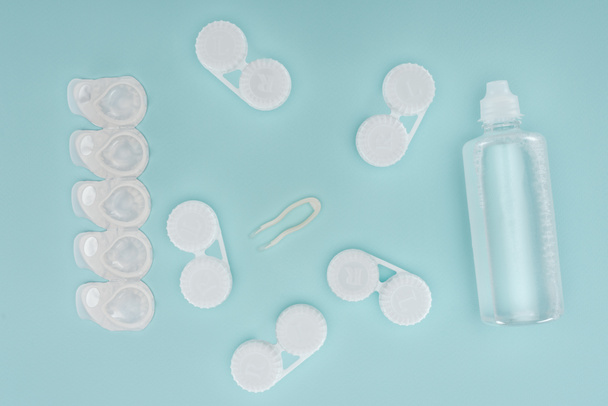 vlakke leggen met steriele vloeistof in fles, pincet en containers voor de opslag van de contactlenzen op blauwe tafelblad - Foto, afbeelding