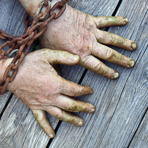 Mans ruce zřetězené s starý rezavý tlustý řetěz na dřevěných desek - Fotografie, Obrázek