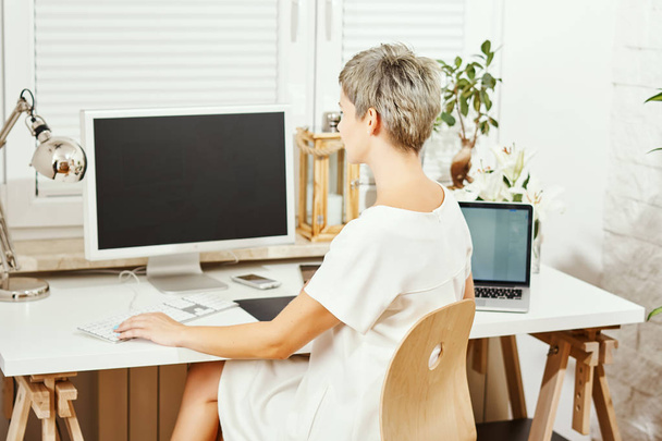 beautiful business woman in white dress sitting at desk and working on computer at home office - Photo, Image