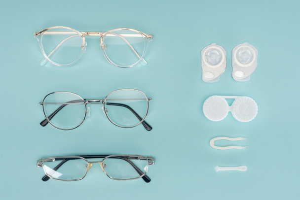 top view of eyeglasses, contact lenses containers and tweezers arranged on blue background - Photo, Image
