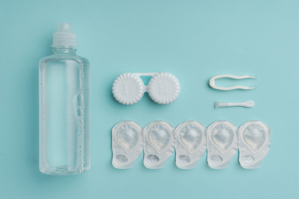 flat lay with sterile liquid in bottle, tweezers and containers for contact lenses on blue tabletop - Photo, Image