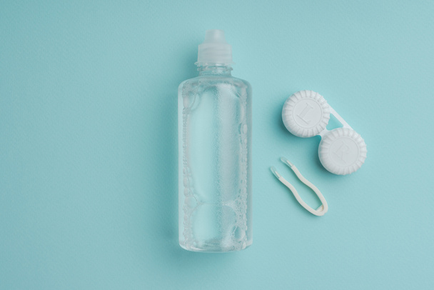 вид сверху на стерильную жидкость в бутылке, пинцете и контейнере для контактных линз на голубом столе
 - Фото, изображение