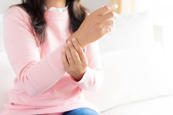 Closeup woman sitting on sofa holds her wrist hand injury, feeling pain. Health care and medical concept. - Photo, Image
