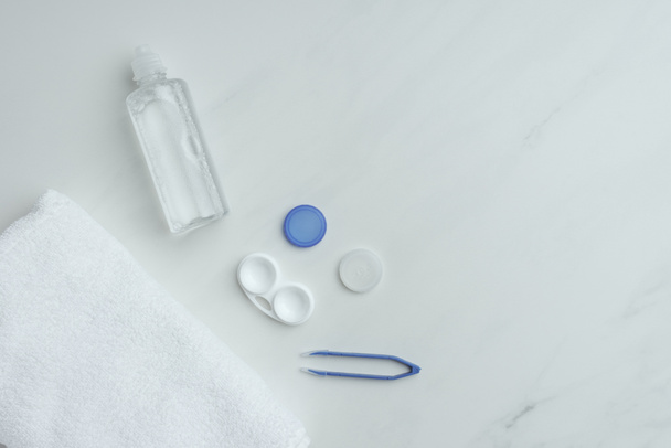 flache Liege mit Handtuch, Kontaktlinsenaufbewahrungsgeräte auf weißer Tischplatte angeordnet - Foto, Bild