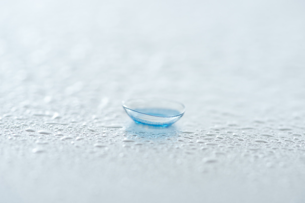 Nahaufnahme der Kontaktlinse auf weißem Hintergrund mit Wassertropfen - Foto, Bild