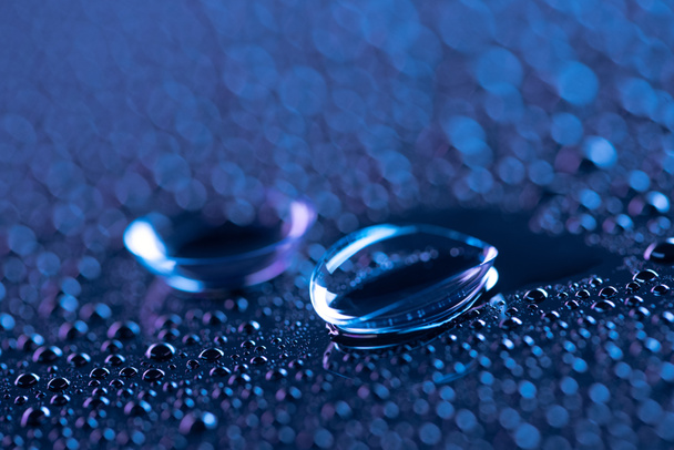 enfoque selectivo de lentes de contacto y gotas de agua sobre fondo azul
 - Foto, imagen